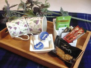 Ein Tablett mit einer Tasse mit Blumenmuster, einer weißen Tasse, einer Milchkaraffe, einer Packung Kekse, einer Packung Keksgebäck und einer Schachtel Pfefferminzbonbons.