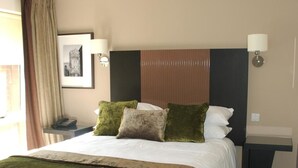 Een hotelkamer met een groot bed, een nachtkastje, een lamp en een ingelijst kunstwerk aan de muur.