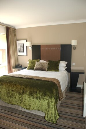 A hotel room with a large bed, a nightstand, a lamp, and a framed picture on the wall. - Staverton Park Hotel and Golf Club (Daventry)