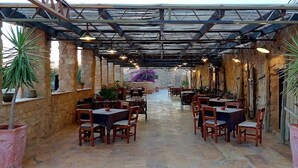 Un espace extérieur aménagé en terrasse, avec des murs en pierre, des tables et des chaises en bois, et des plantes en pot.