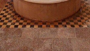 Une salle de bain avec un lavabo circulaire central, un carrelage à motifs géométriques et de petites fenêtres aux encadrements verts et blancs.