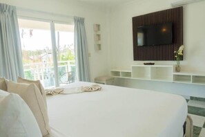 A hotel room with a large bed, a TV mounted on a wooden panel, a balcony with a view, and a small table. - Green Coast Hotel Punta Cana (Punta Cana)