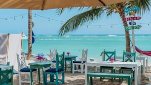 Een zitgedeelte aan het strand met tafels, stoelen, een hangmat en een bord met wegwijzers.