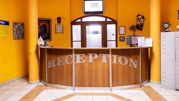 A reception area with a wooden reception desk, a television mounted above the desk, and a clock on the wall. - Sunrise Complex Hotel (Nessebar)