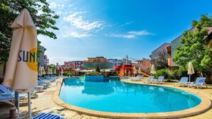 A swimming pool with lounge chairs and umbrellas, surrounded by buildings. - Sunrise Complex Hotel (Nessebar)