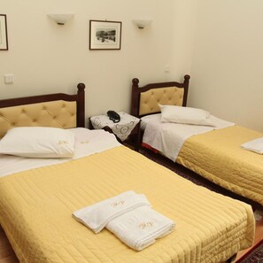 A hotel room with two beds, each with a yellow quilted bedspread and white pillows, and a small bedside table with a lamp. - Hotel Panellinion (Trikala)