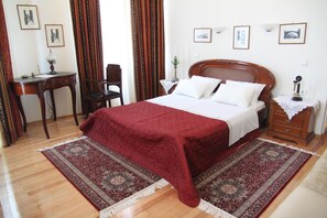A hotel room with a wooden bed, a desk, a chair, and a nightstand with a lamp. - Hotel Panellinion (Trikala)