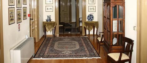 A hallway with a patterned rug, a wooden cabinet with a picture frame, and a ceiling light fixture.