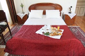A neatly made bed with a red bedspread, a tray of breakfast items, and a nightstand with a lamp. - Hotel Panellinion (Trikala)