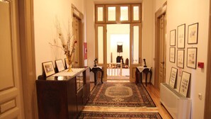 A hallway with a patterned rug, wooden furniture, and framed pictures on the walls. - Hotel Panellinion (Trikala)