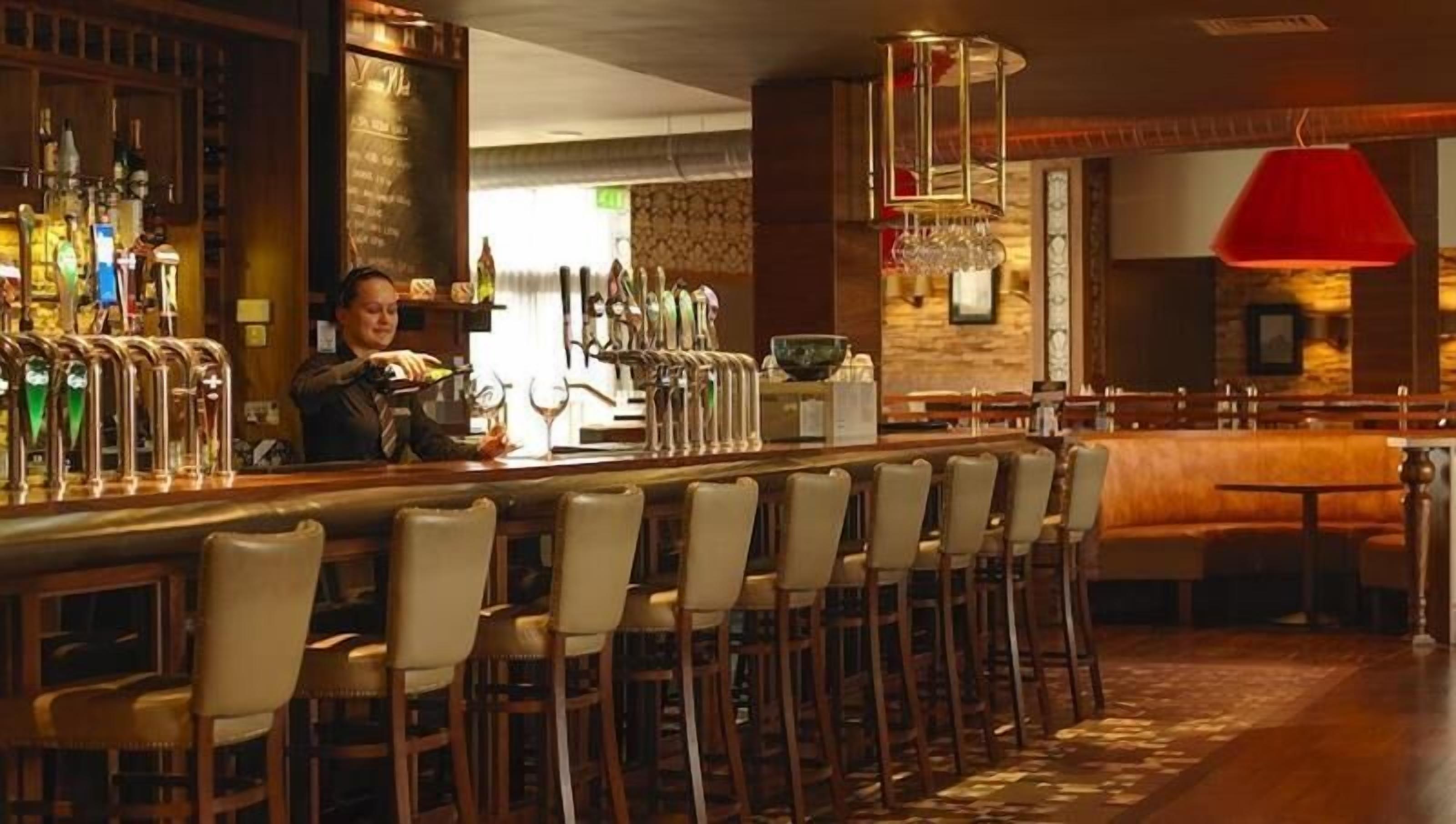 Een bar met een bartender, meerdere tappunten en een rode hanglamp.