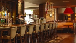 Zona de bar con un bartender, varias griferías y una lámpara colgante roja.