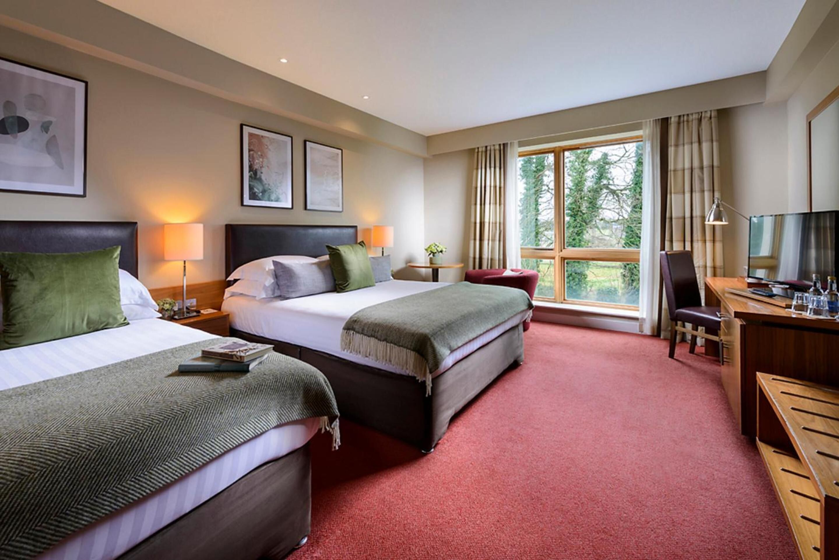 A hotel room with two beds, a desk, a chair, a TV, and a window with curtains.