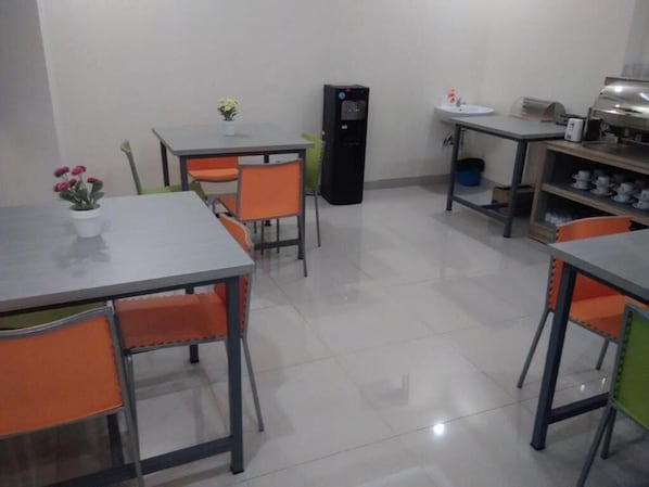 Un comedor con mesas y sillas, un refrigerador, un lavamanos y una estación de buffet.