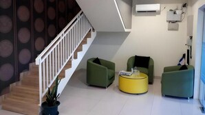 Un salon moderne avec un escalier, des canapés verts, une table basse jaune et un appareil de climatisation fixé au mur.
