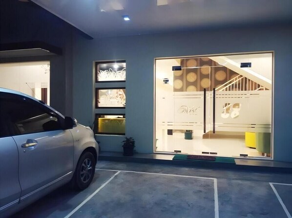 Un edificio moderno con fachada de vidrio, un coche estacionado al frente y una escalera que sube a un nivel superior.