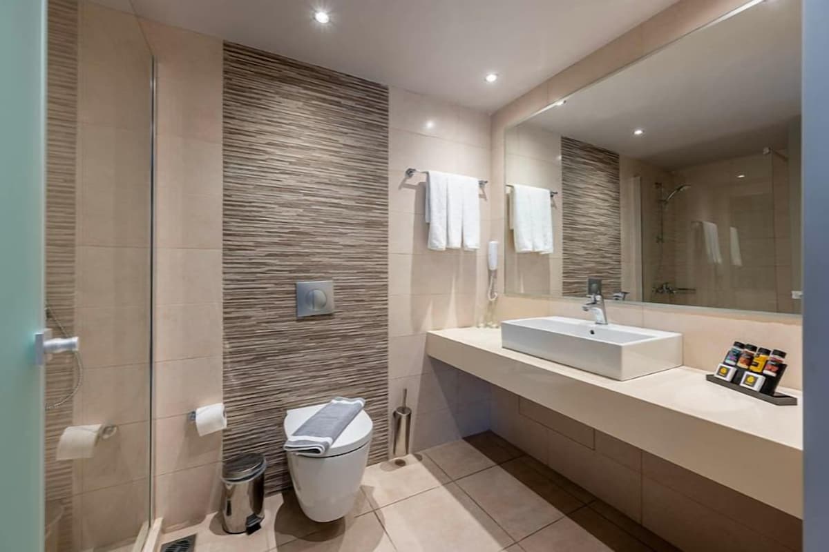 Une salle de bain moderne équipée d’une douche, de deux lavabos, de toilettes et d’un grand miroir.