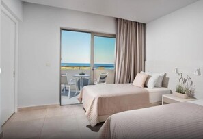 A hotel room with two beds, a balcony with a view of the sea, a small table, and a chair. - Porto Bello Beach (Kos)