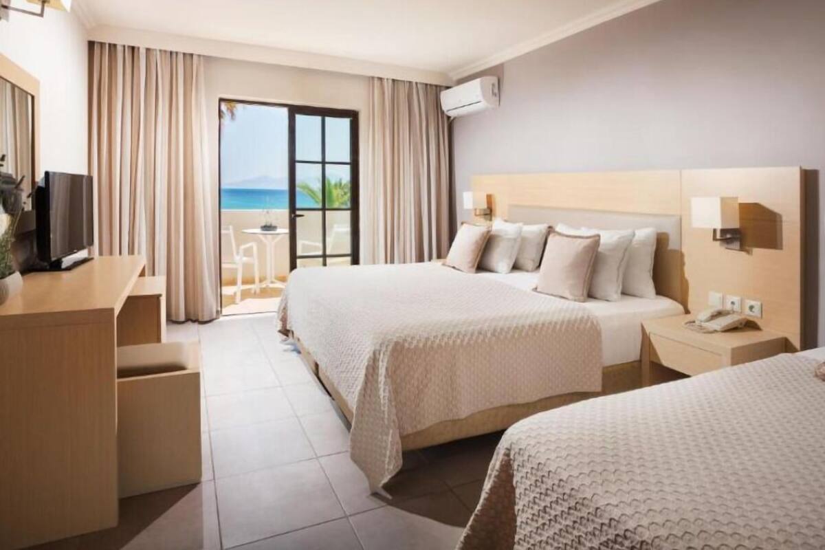 Habitación de hotel con dos camas, un escritorio, televisor y vista al océano.