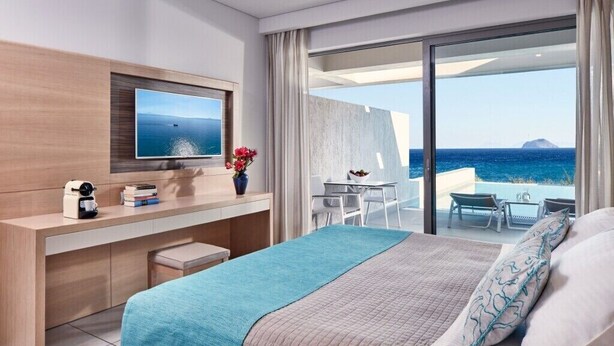 Ein modernes Hotelzimmer mit Bett, Schreibtisch, Fernseher und einem Balkon mit Meerblick.