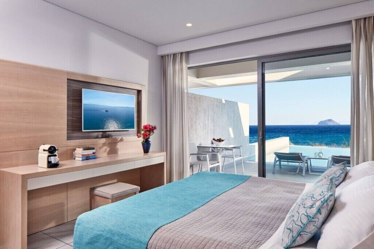 Habitación de hotel moderna con cama, escritorio, televisión y balcón con vista al mar.