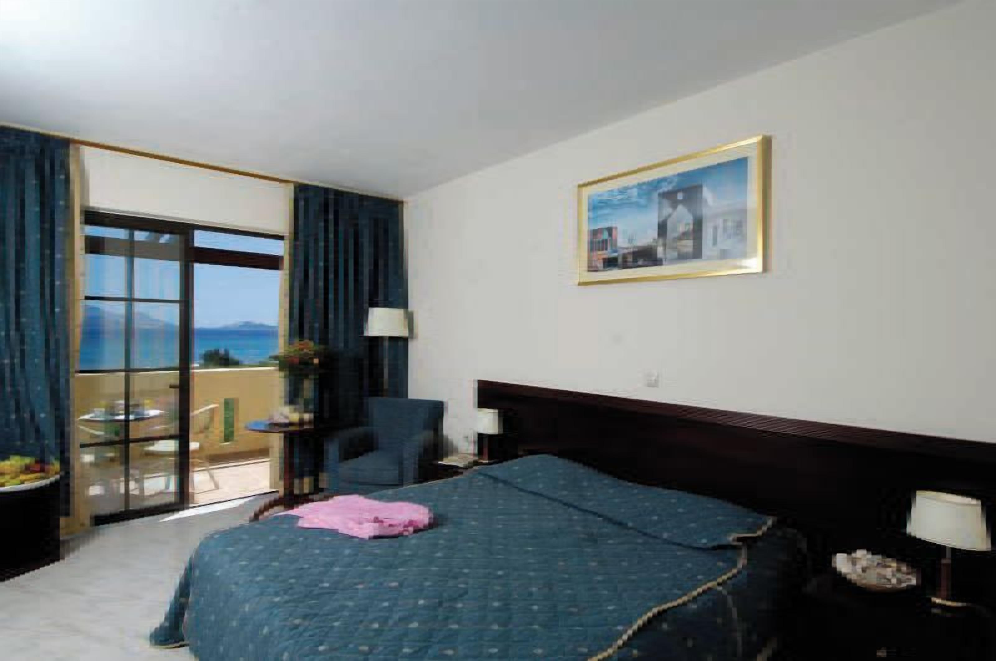 A hotel room with a bed, a chair, a table, a lamp, and a view of the outdoors.