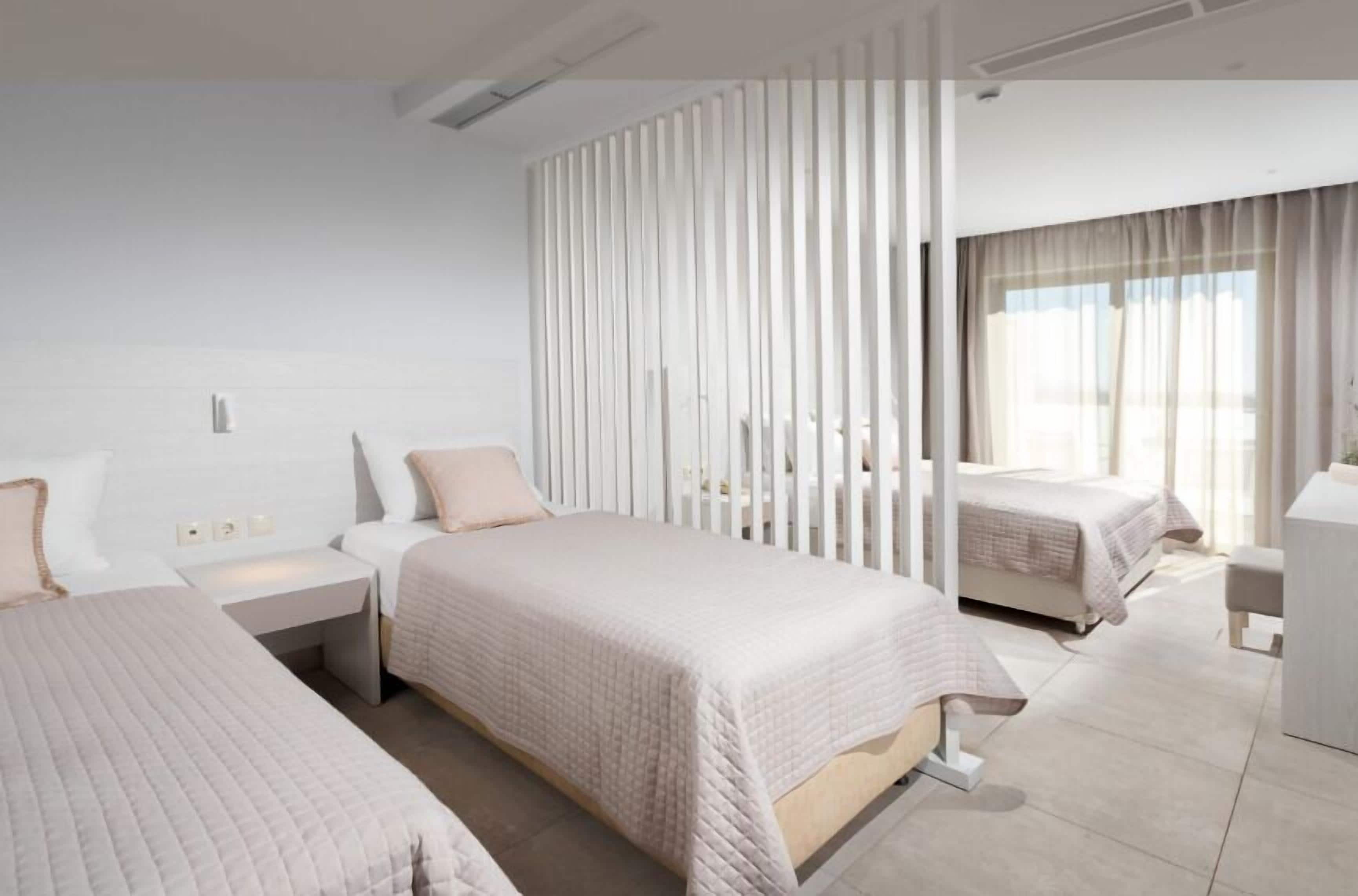 A modern hotel room with two beds, a large window, and a white color scheme.