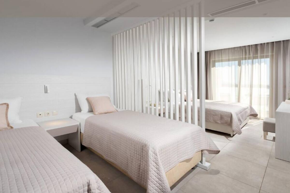 Una habitación de hotel moderna con dos camas, un ventanal grande y una decoración en tonos blancos.