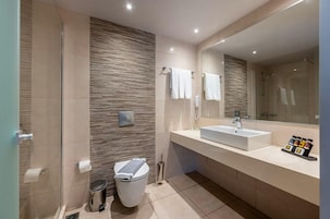 Un baño moderno con ducha, dos lavamanos, inodoro y un espejo grande.