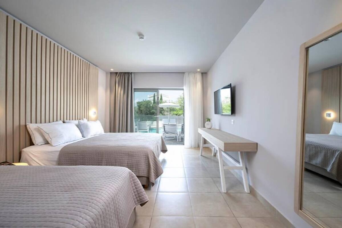 Habitación de hotel con dos camas, un escritorio, televisión y balcón con mobiliario exterior.