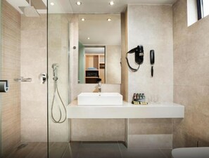 A modern bathroom with a glass shower enclosure, a white sink, and a mirror reflecting a walk-in closet. - Porto Bello Beach (Kos)