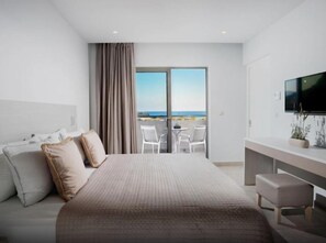 Une chambre d’hôtel moderne dotée d’un grand lit, d’une télévision, d’un balcon avec vue sur la mer et d’un espace bureau.