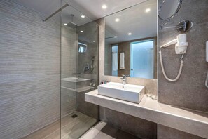Une salle de bain moderne dotée d’une douche à parois de verre, d’un grand miroir et d’un lavabo intégré.