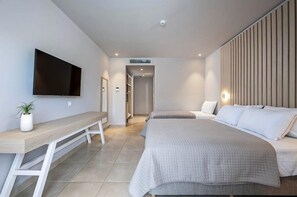 Une chambre d’hôtel moderne équipée d’une télévision à écran plat, d’un banc en bois, de deux lits, d’une plante en pot et d’un dressing.
