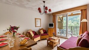Een knus vertrek met een eettafel gedekt voor vier personen, een bank, een televisie en een balkon met uitzicht.