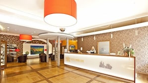 Uma área de recepção de hotel com design moderno, com balcão de atendimento, área de estar e obras de arte nas paredes.