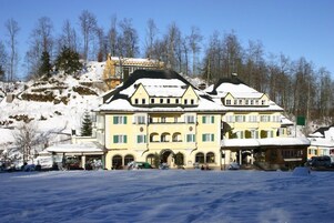 Un edificio grande de varios pisos con techo cubierto de nieve, rodeado de un paisaje nevado y árboles.