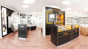 Uma loja moderna com vitrine central para relógios MIDO, rodeada por outras marcas de luxo como Tissot e Cartier.