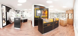 A modern retail store with a central display for MIDO watches, surrounded by other luxury brands like Tissot and Cartier. - Mueller (Schwangau)