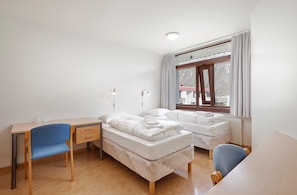 Una habitación con escritorio, dos camas individuales, una silla y una ventana con cortinas.