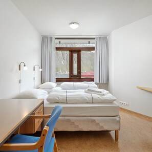 Un dormitorio con cama, escritorio, silla, ventana con cortinas e iluminación en el techo.