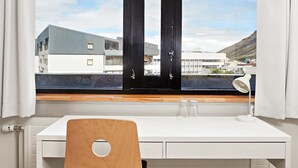 A room with a white desk, a wooden chair, a window with a view of buildings, and a white lamp. - Edda Hotel Isafjorour (Isafjordur)