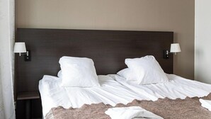 Un letto rifatto con lenzuola bianche e due cuscini, una testiera in legno scuro e due lampade da parete su entrambi i lati.