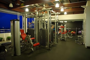 A gym with various exercise machines, a red chair, and a view of the city at night. - Hotel Gajahmada Pontianak (Pontianak)