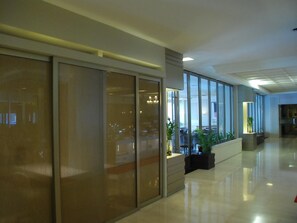 Un interior modern amb un llarg passadís, separadors de vidre i plantes en testos.