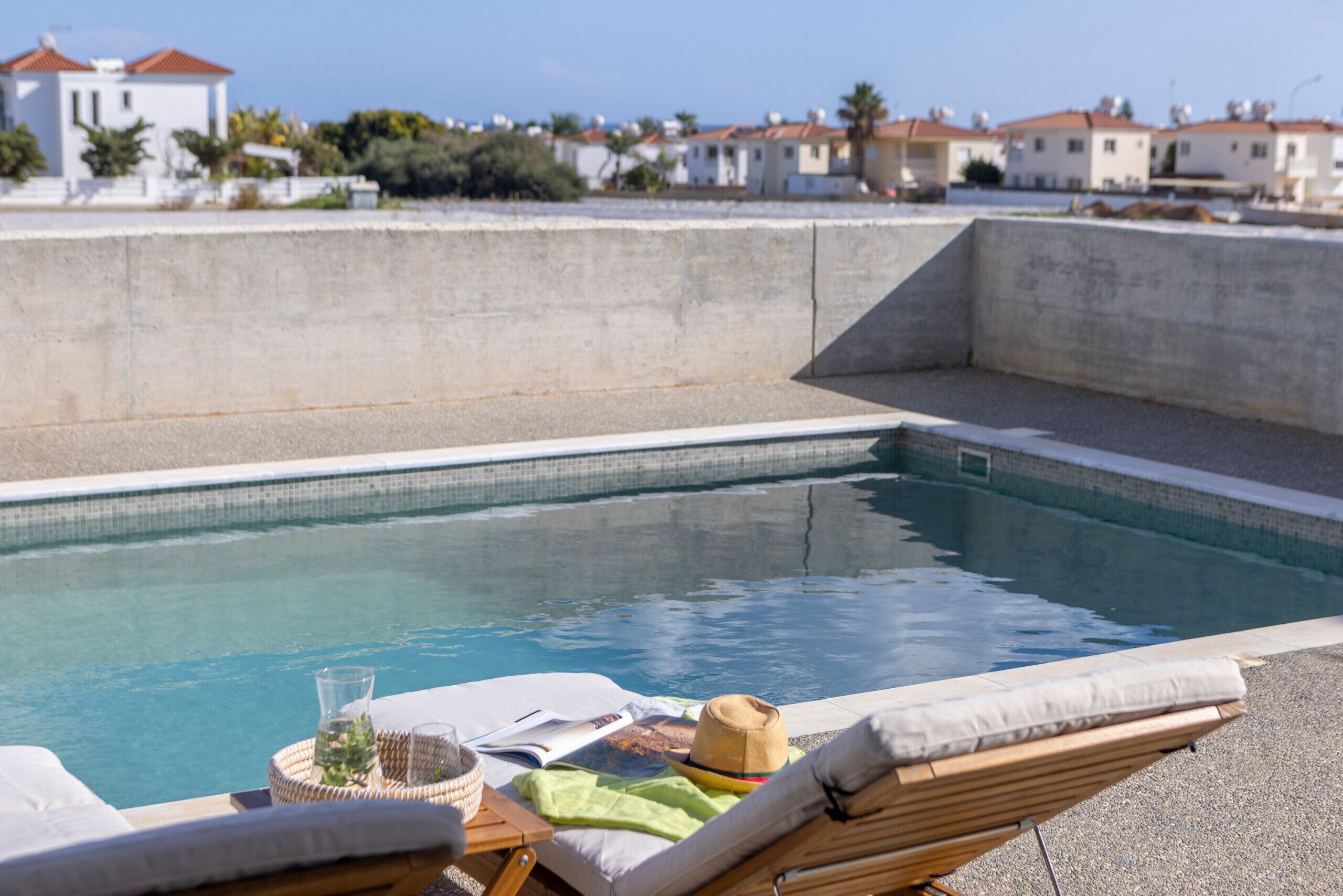 A poolside area with lounge chairs, a small table with a hat, and a book.