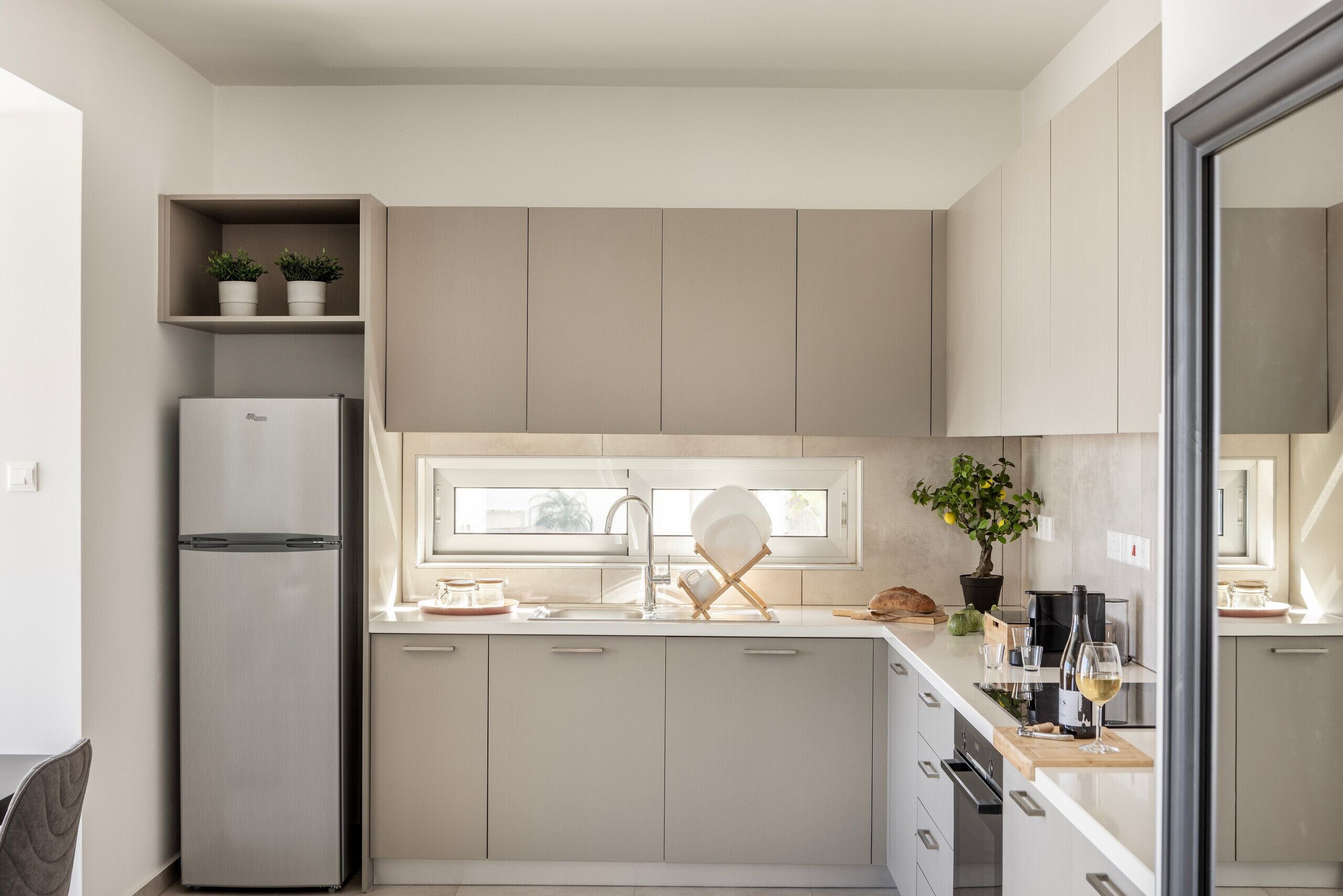 Una cocina moderna con refrigerador empotrado, una ventana sobre el lavamanos y una planta en maceta en la encimera.