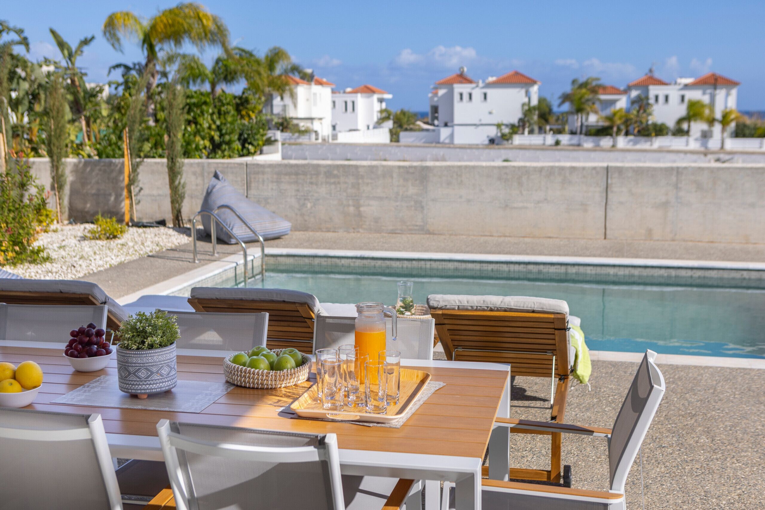 A dining area with a pool view, outdoor seating, and a table set with fruits and drinks.
