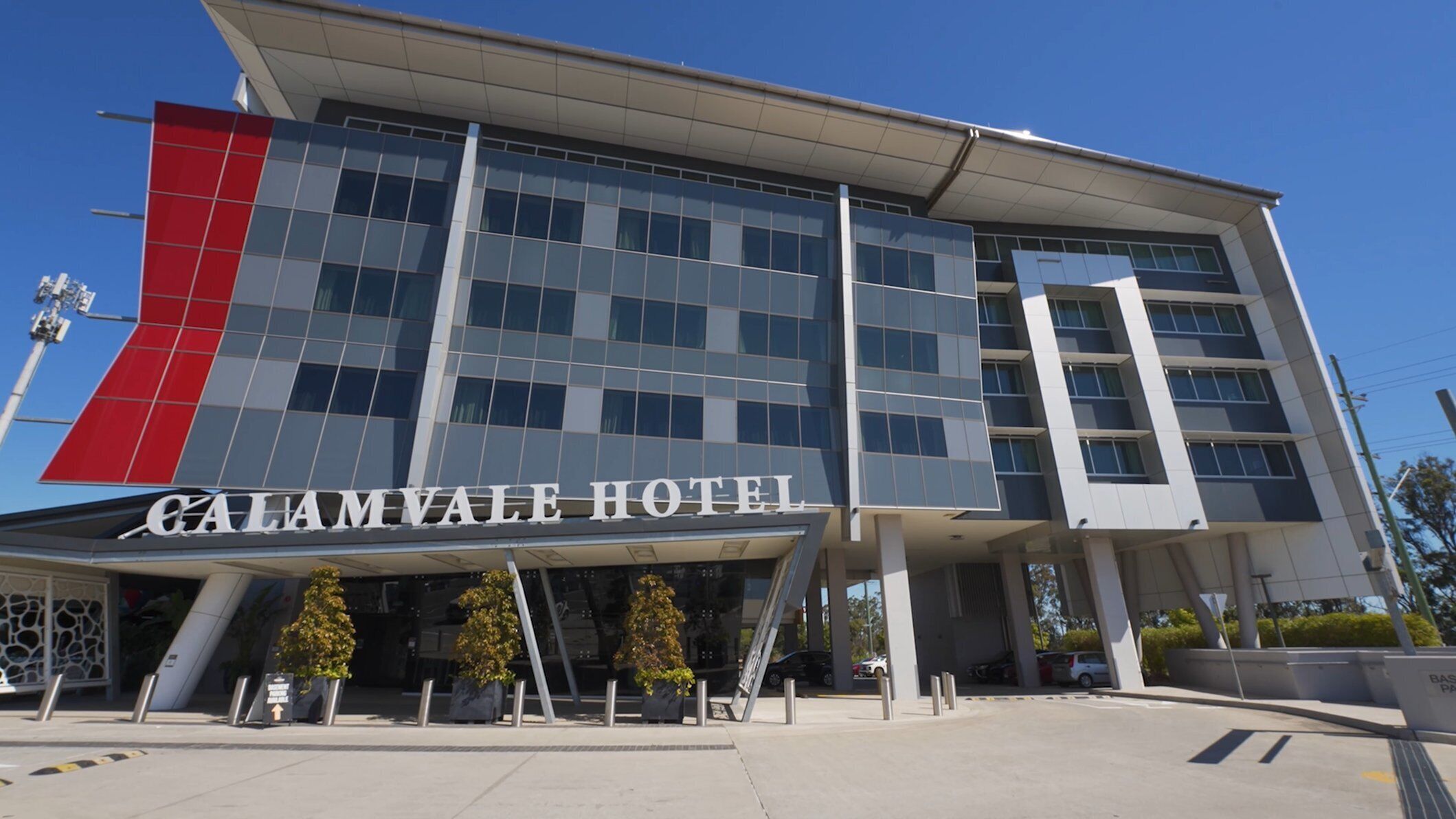A modern hotel building with a prominent red and grey facade, large windows, and a clear sky.
