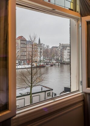 A window view of a canal with buildings and a tree in the foreground. - Hotel Monopole (Amsterdam)